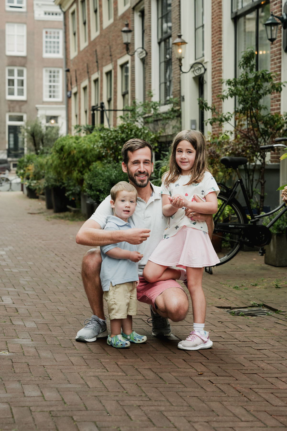 Father crouching beside his two children for a portrait on an Amsterdam street.