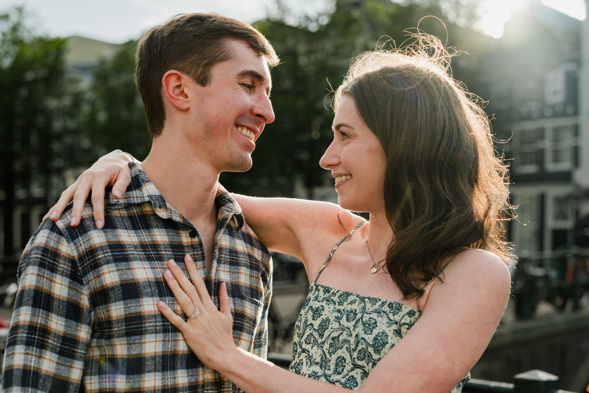 Newly engaged couple smiling together beside an Amsterdam canal after their proposal.