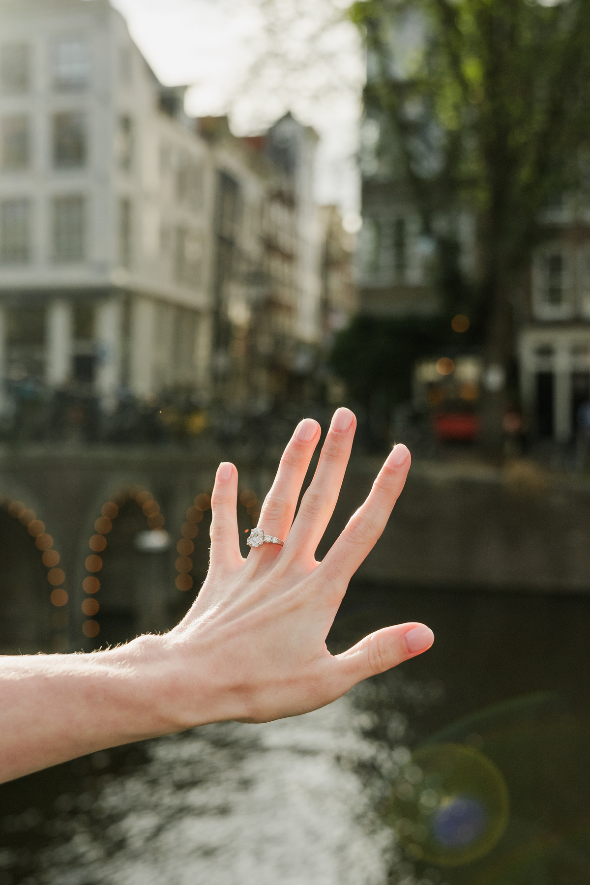 Close-up of an engagement ring held up beside an Amsterdam canal.
