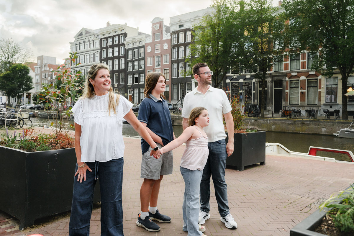 Happy family smiling during their photo session in Amsterdam next to a canal with boats and historical houses in the background 