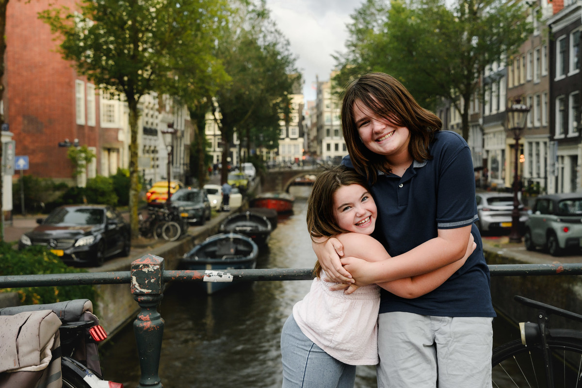 Siblings standing on a bridge with a beautiful canal and historical houses in the background. This was during their family photo session in Amsterdam. 