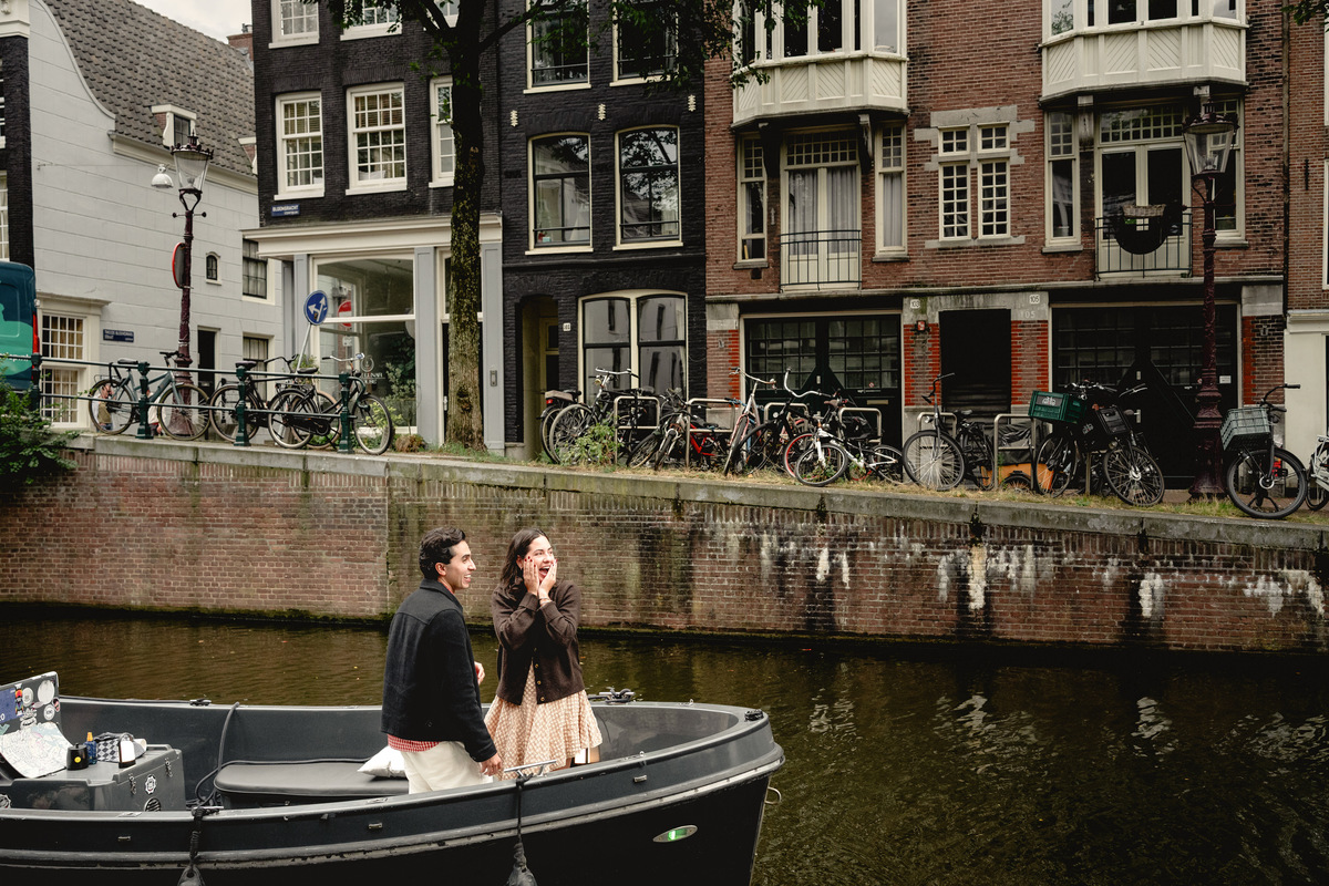 Engaged couple on an open boat beside Amsterdam canal houses.