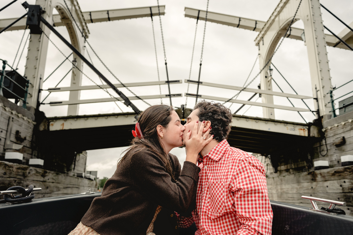 Engaged couple kissing beneath a bridge on an Amsterdam boat.