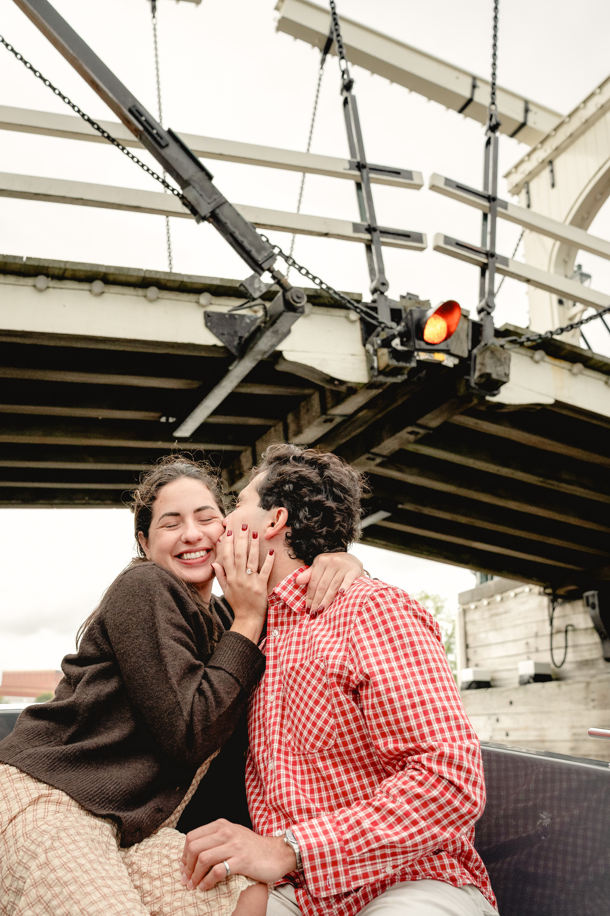 Couple smiling together as their boat passes beneath an Amsterdam bridge.

