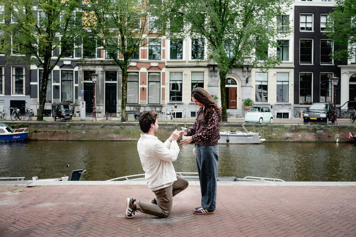 Man proposing on one knee beside an Amsterdam canal.