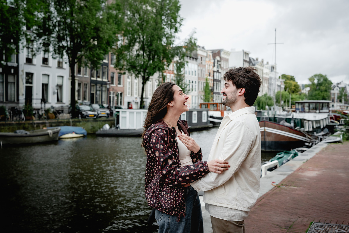 Newly engaged couple embracing beside a peaceful Amsterdam canal.