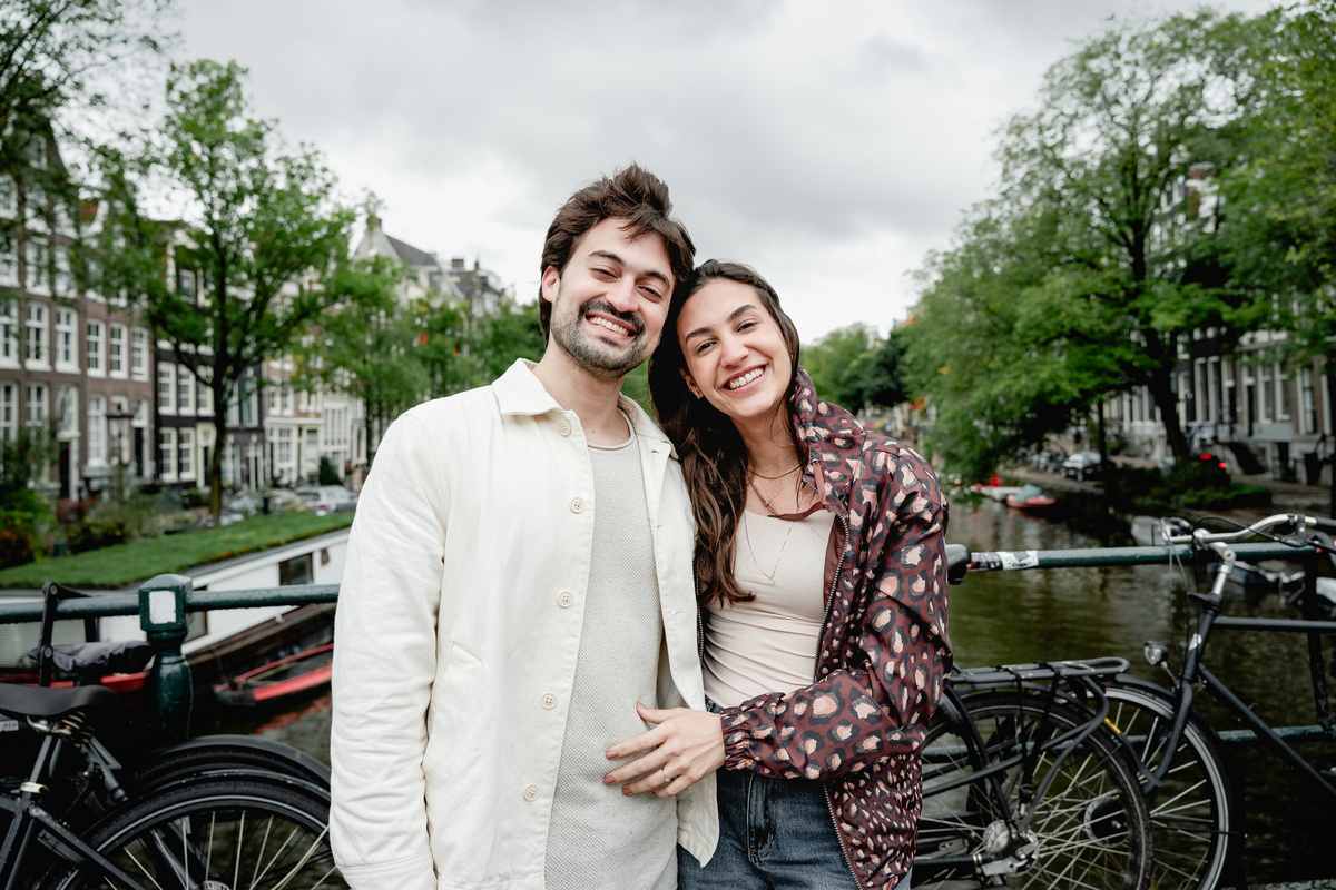 Smiling newly engaged couple on an Amsterdam canal bridge.