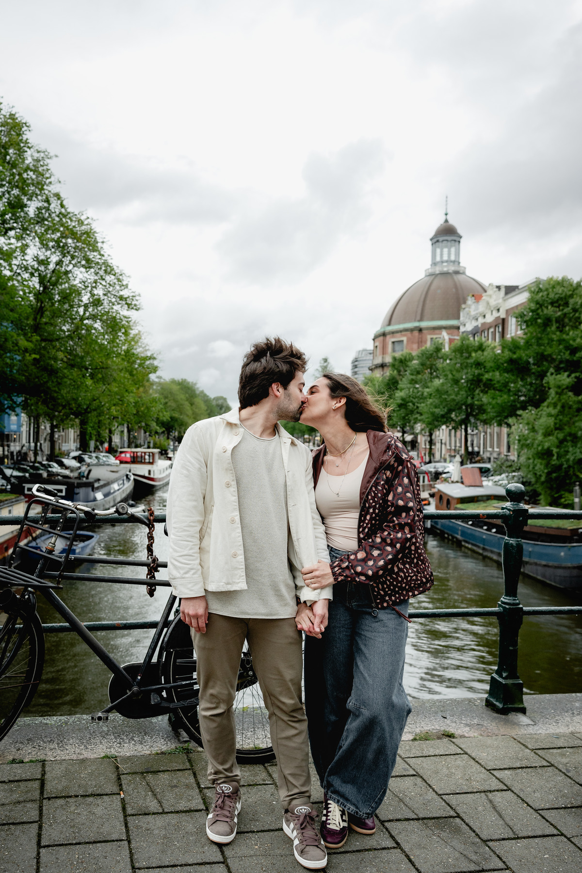 Couple walking beside a canal with Amsterdam church towers in the background.
