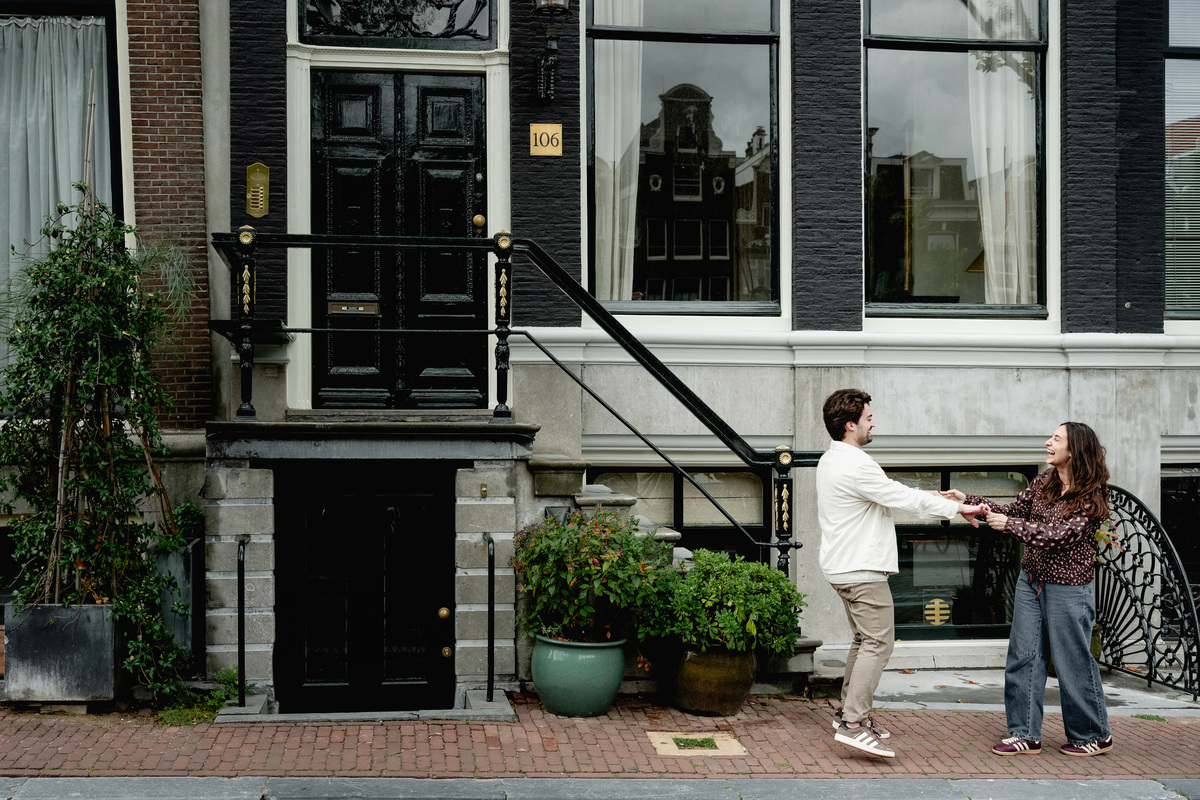 Newly engaged couple walking along an Amsterdam street beside canal houses.