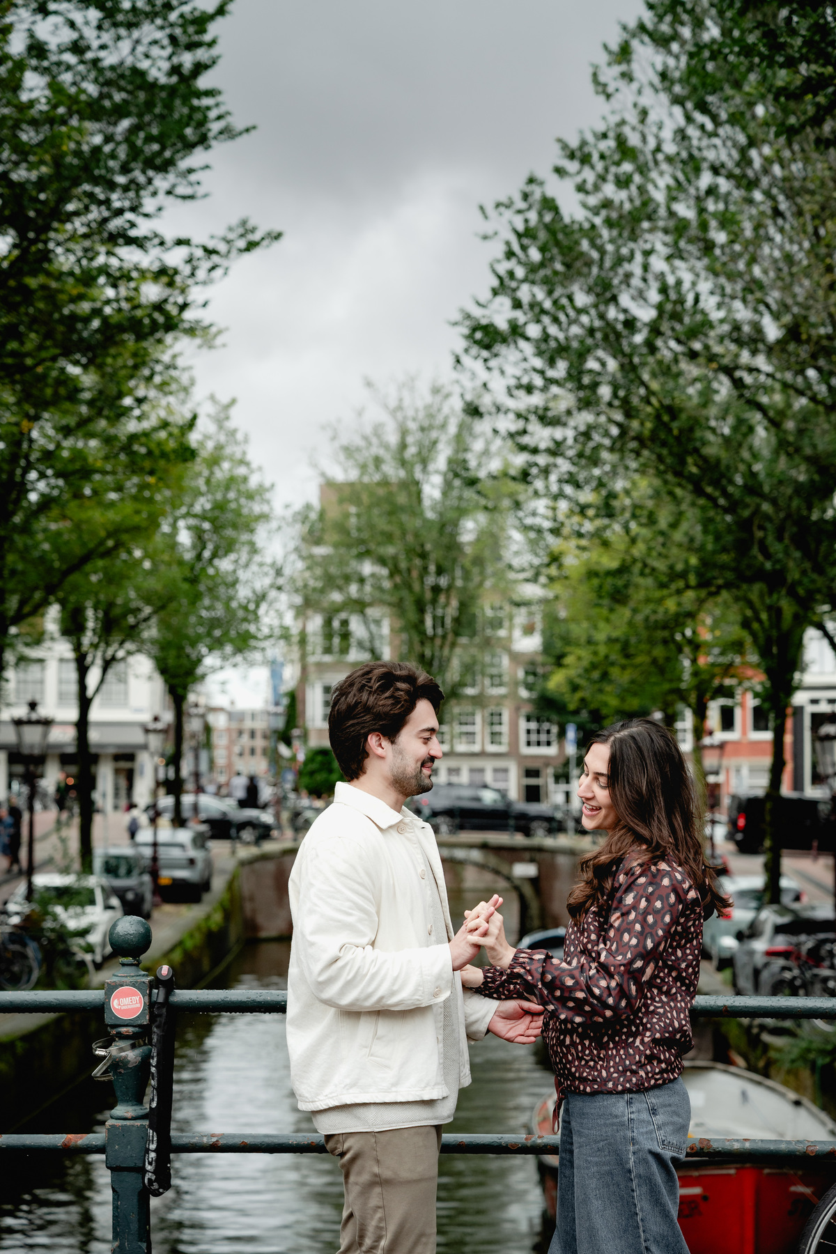Engaged couple smiling together during a canal-side walk in Amsterdam.