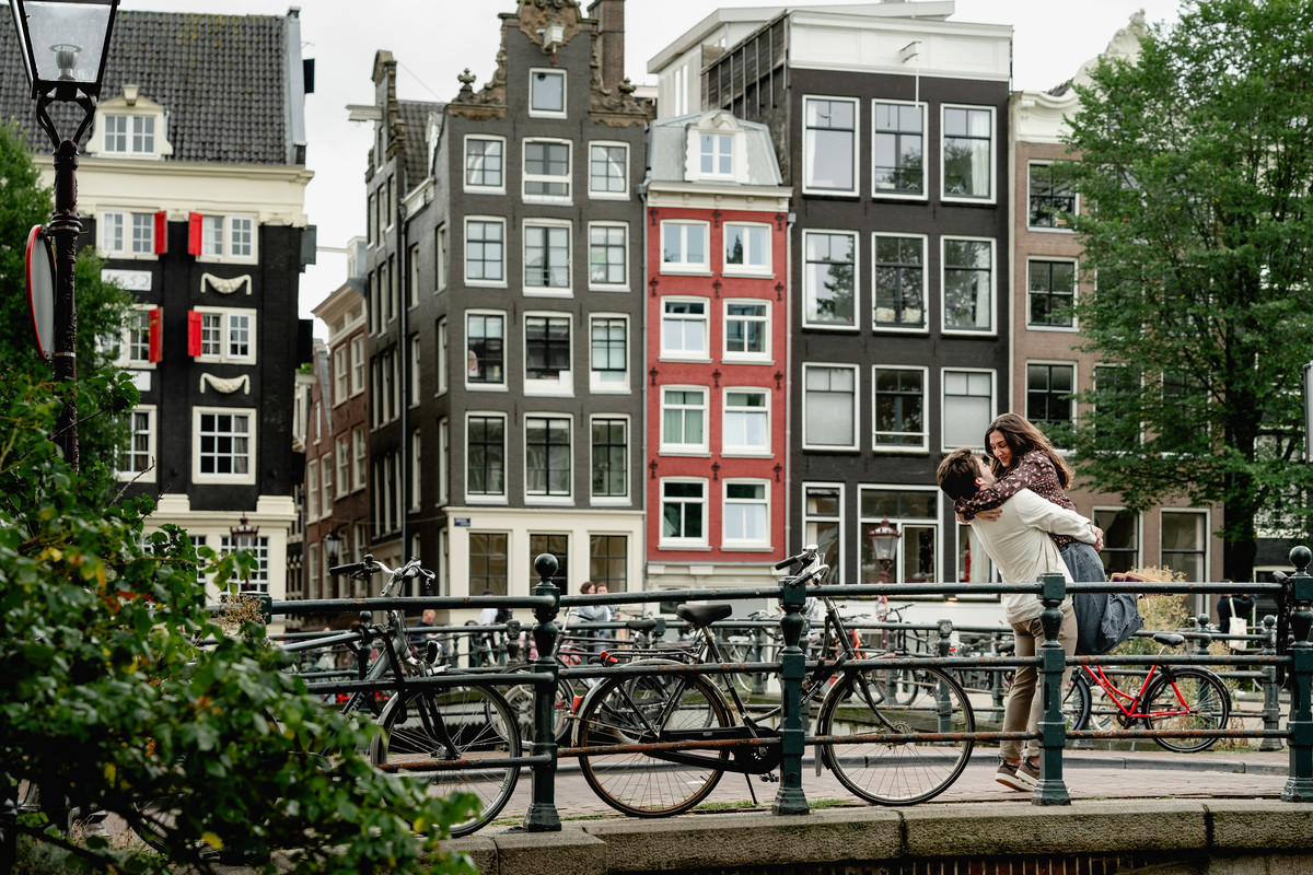 Couple walking across a bridge with Amsterdam canal houses behind them.