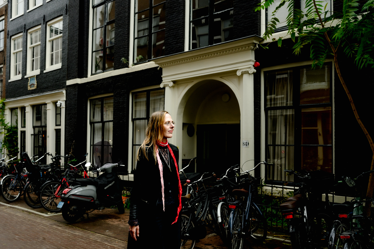 Woman standing beside historic Amsterdam canal houses during a solo photo session.
