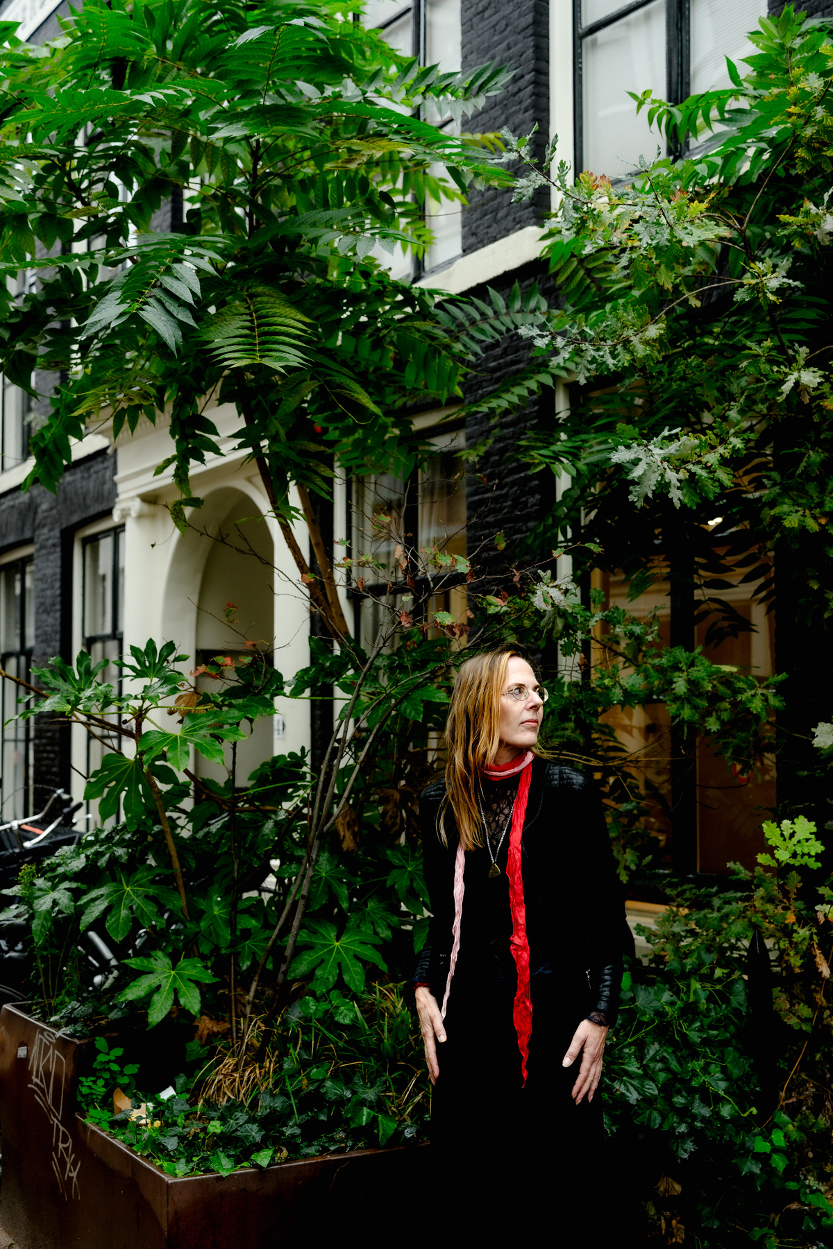 Woman in a red scarf standing beneath green trees during an Amsterdam portrait session.