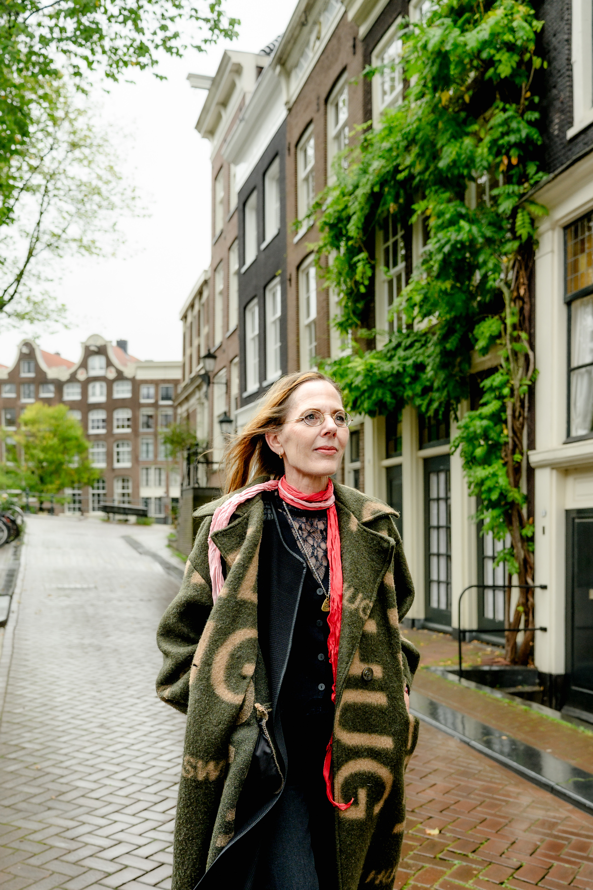 Woman in a red scarf walking beside Amsterdam canal houses.