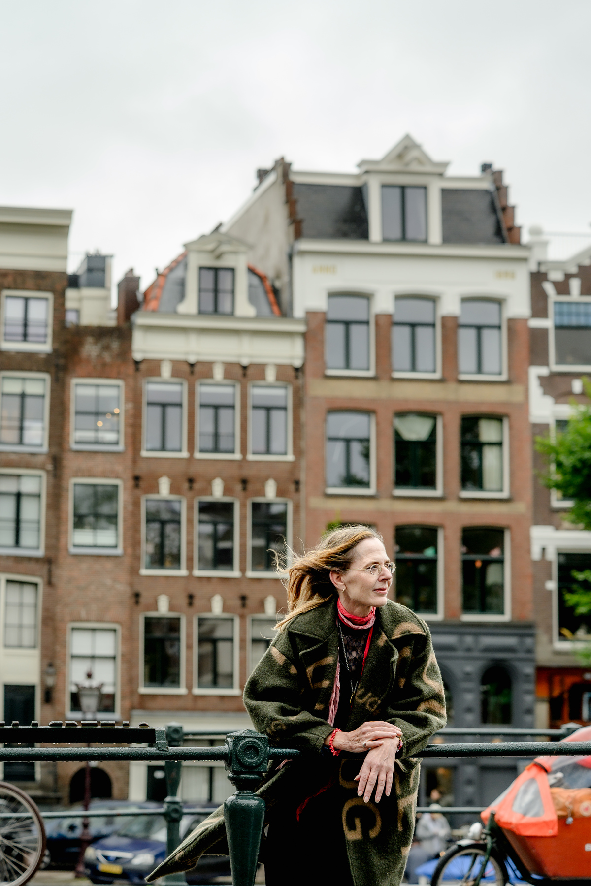 Woman standing near a canal with Amsterdam houses behind her.