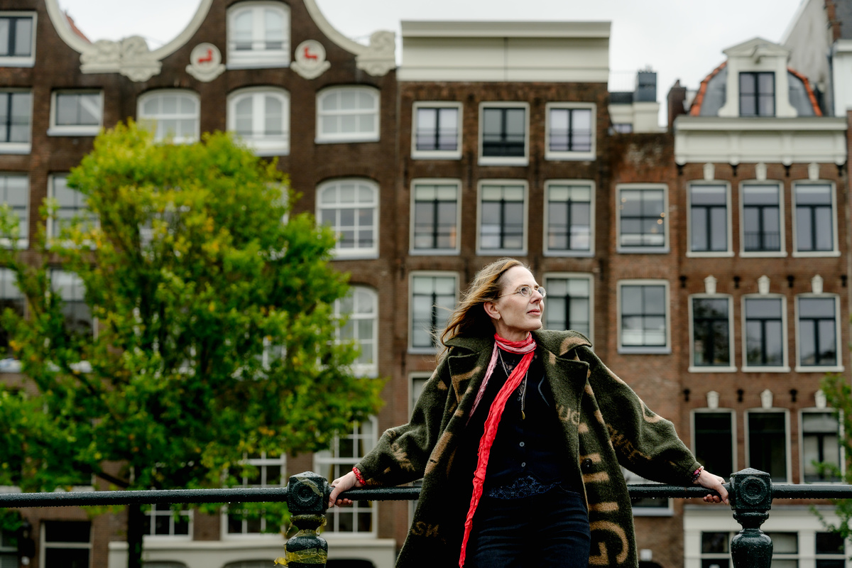 Woman in a red scarf photographed beside Amsterdam canal houses.