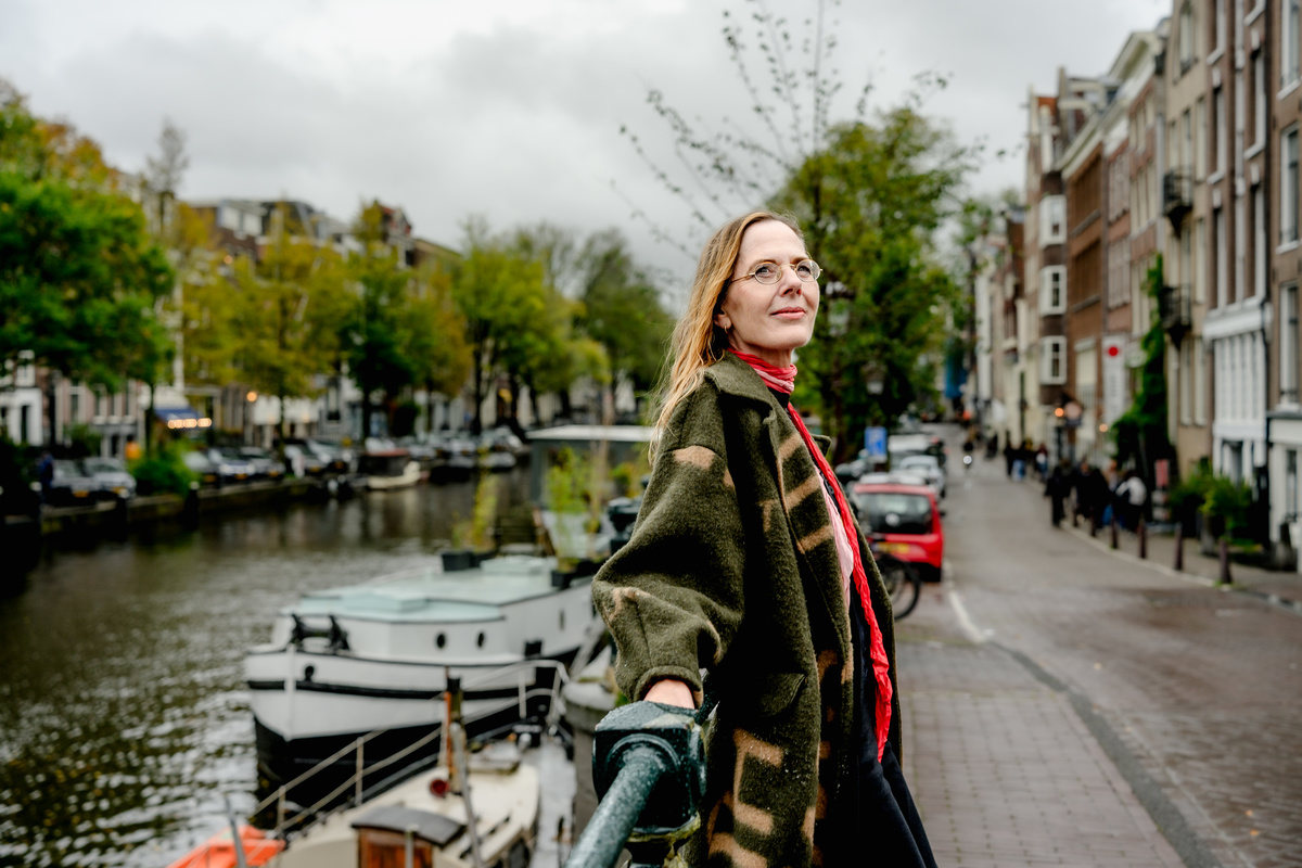 Woman walking along an Amsterdam canal with historic houses behind her.