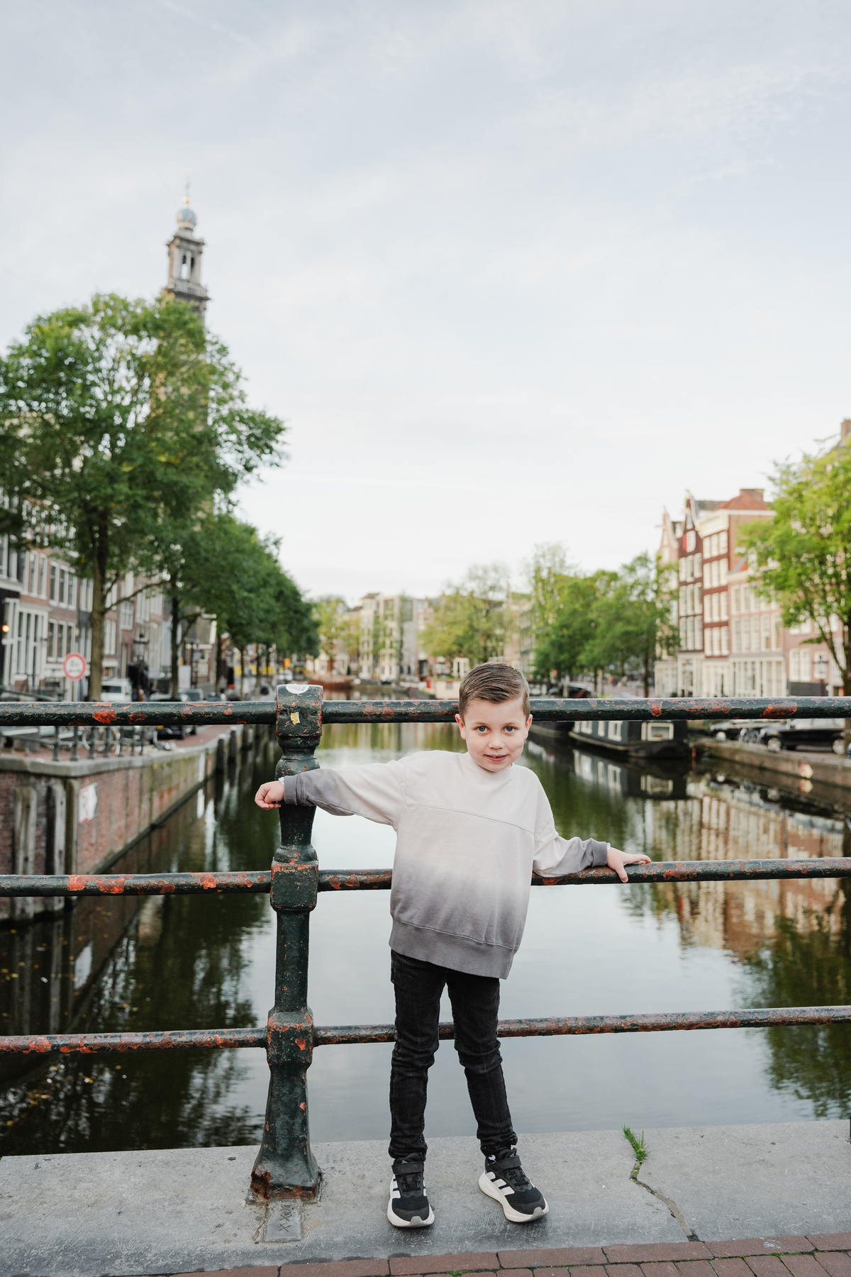 Child standing on a canal bridge with Amsterdam in the background.