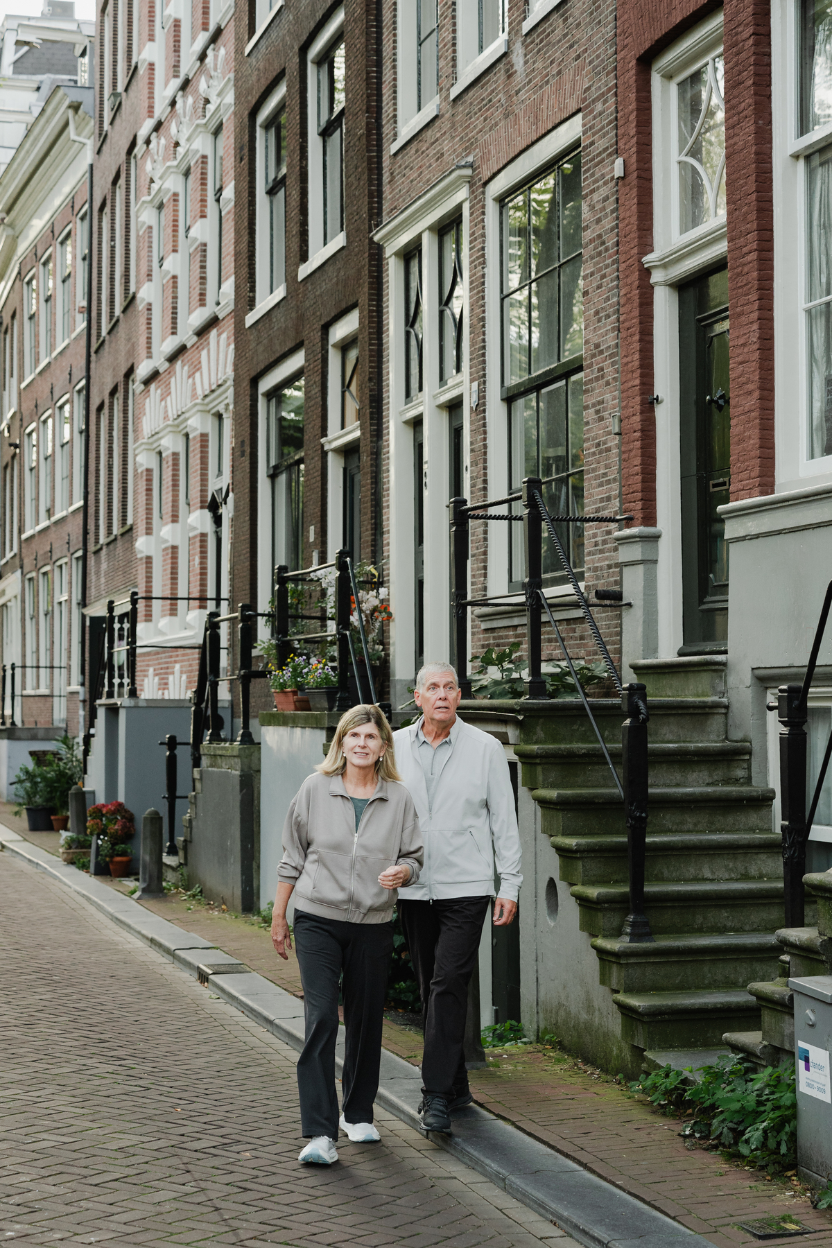 Grandparents walking together beside historic Amsterdam canal houses.