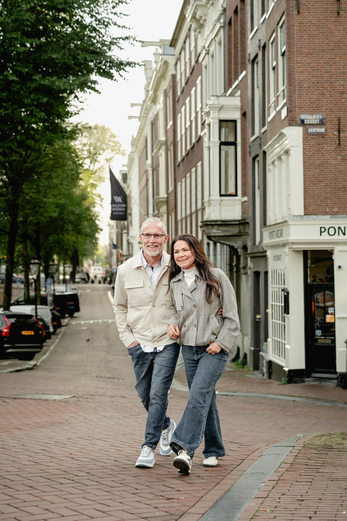 Couple holding hands while walking past traditional Amsterdam houses.