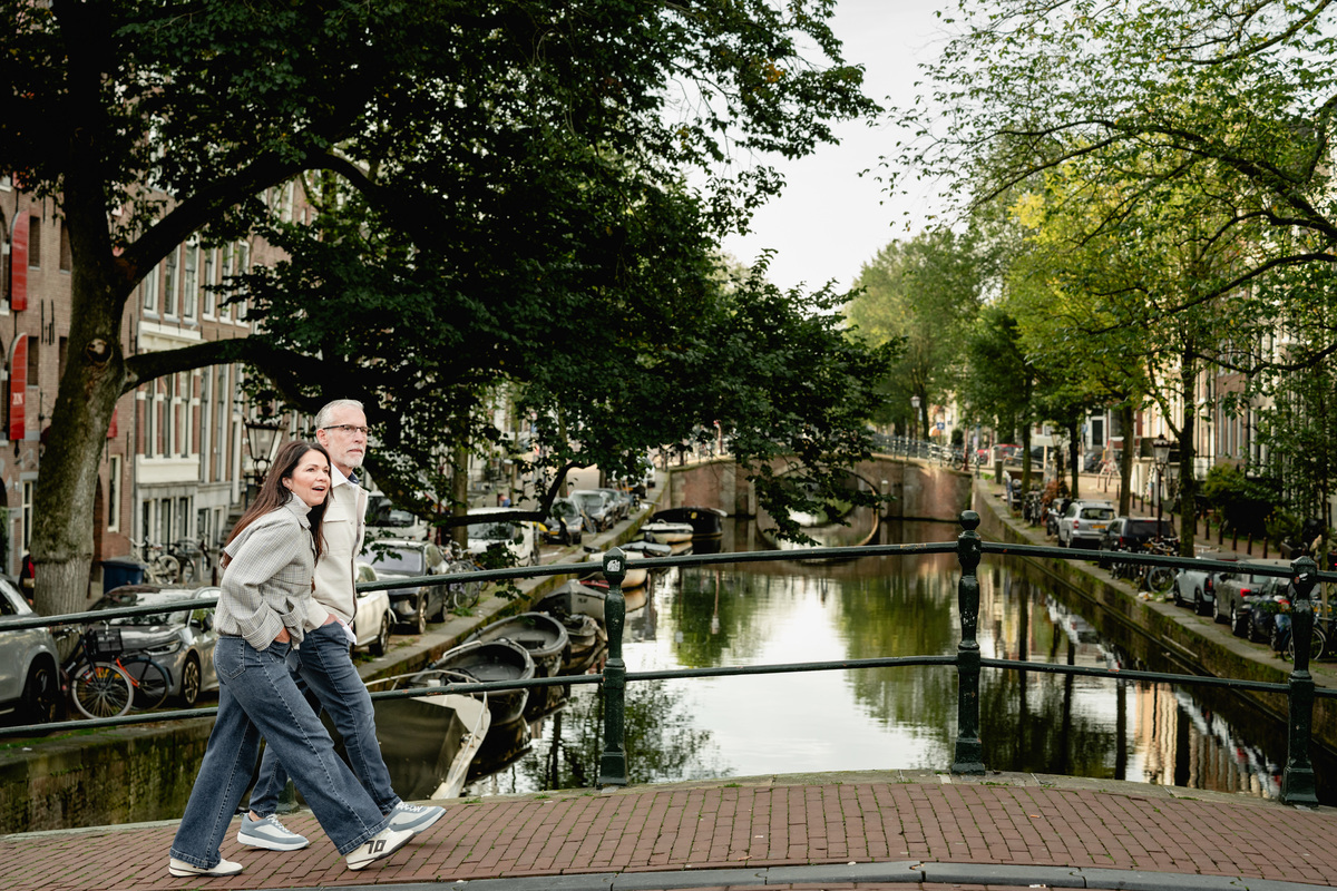 Woman walking beside an Amsterdam canal lined with trees and historic homes.