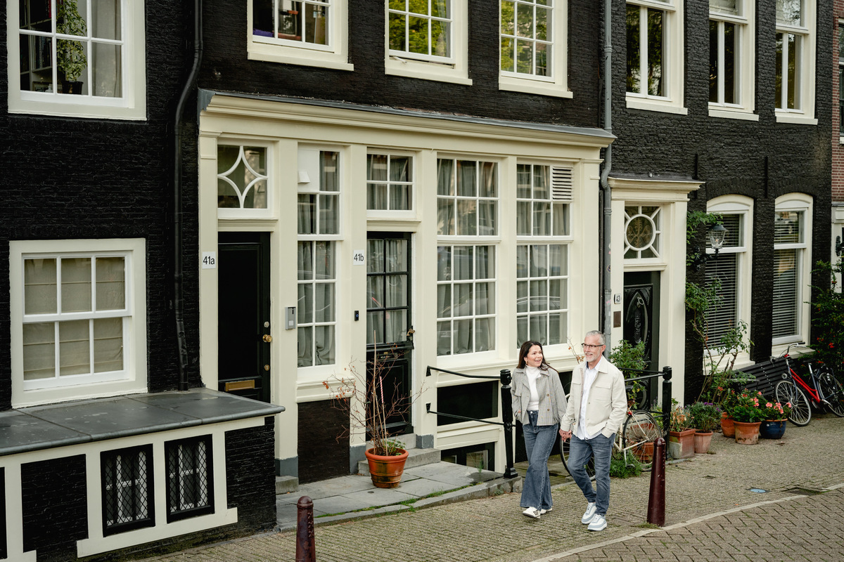 Wide view of a couple standing in front of classic Amsterdam canal houses.