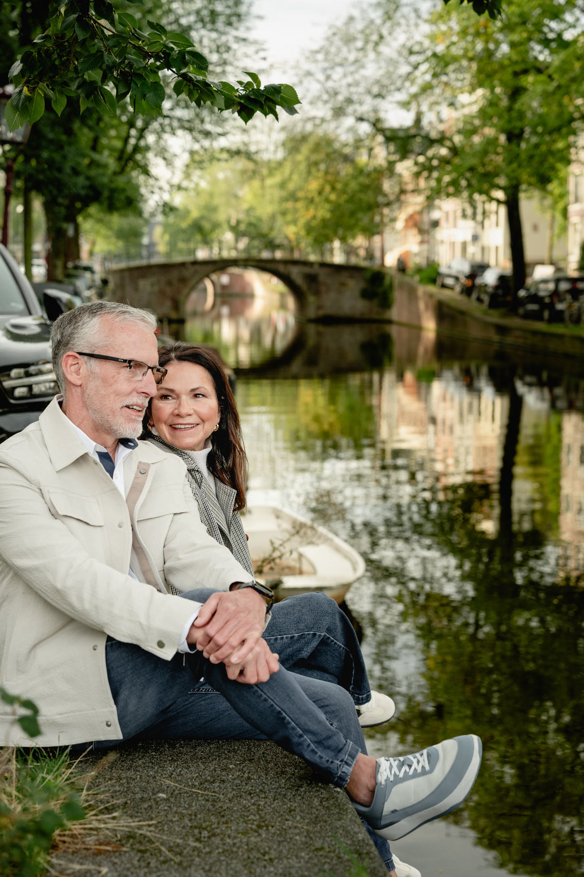 Couple sitting close together beside a tree-lined canal in Amsterdam.