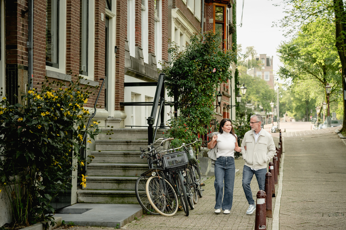 Couple walking down a calm Amsterdam street with bicycles and canal houses.