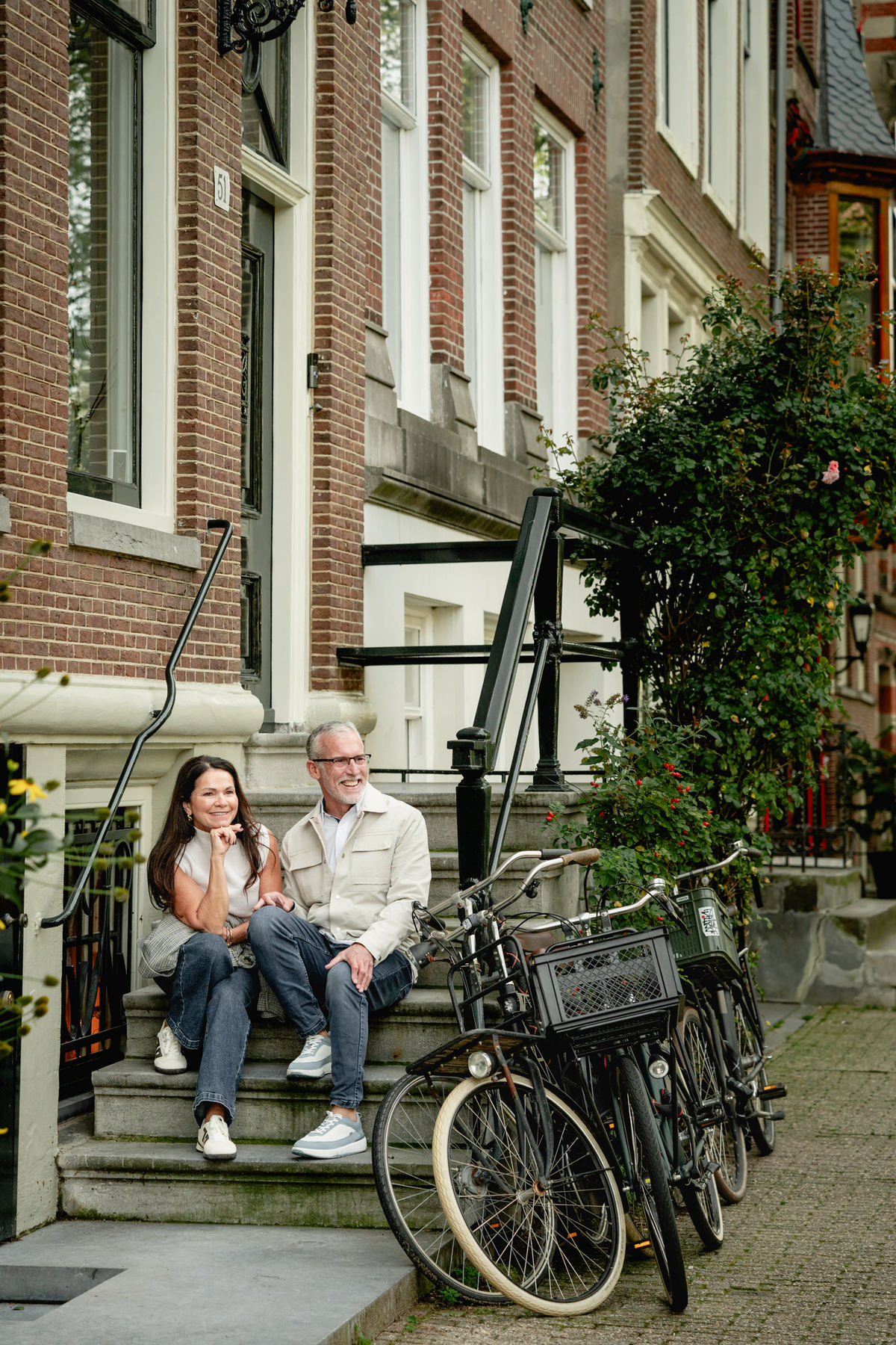 Couple sitting on steps beside bicycles during a natural Amsterdam couple photo session.