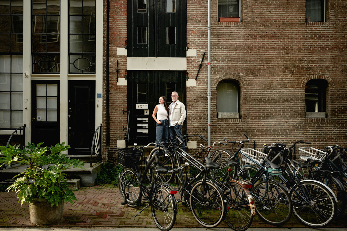 Couple standing by bicycles outside historic Amsterdam canal houses.