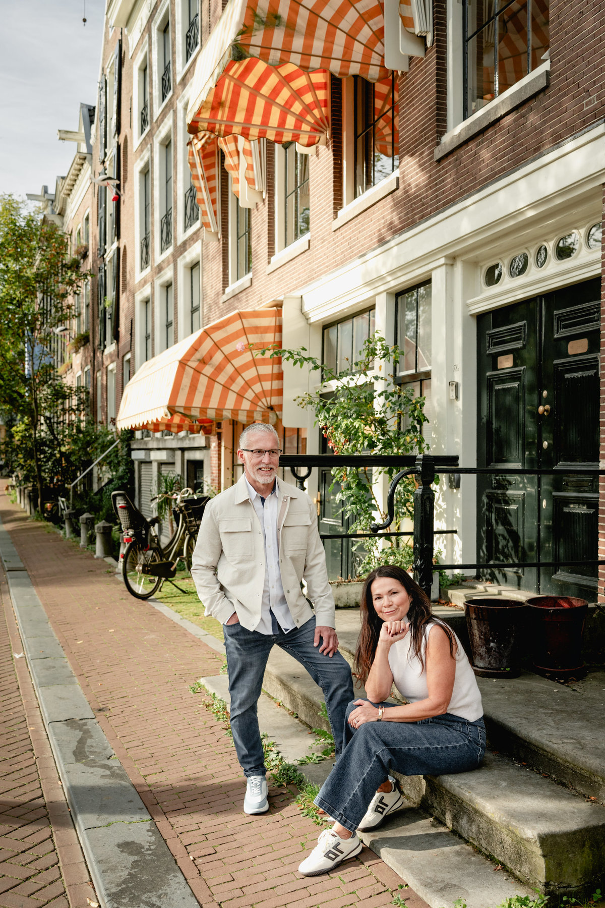 Couple by a striped awning and canal house steps in Amsterdam.
