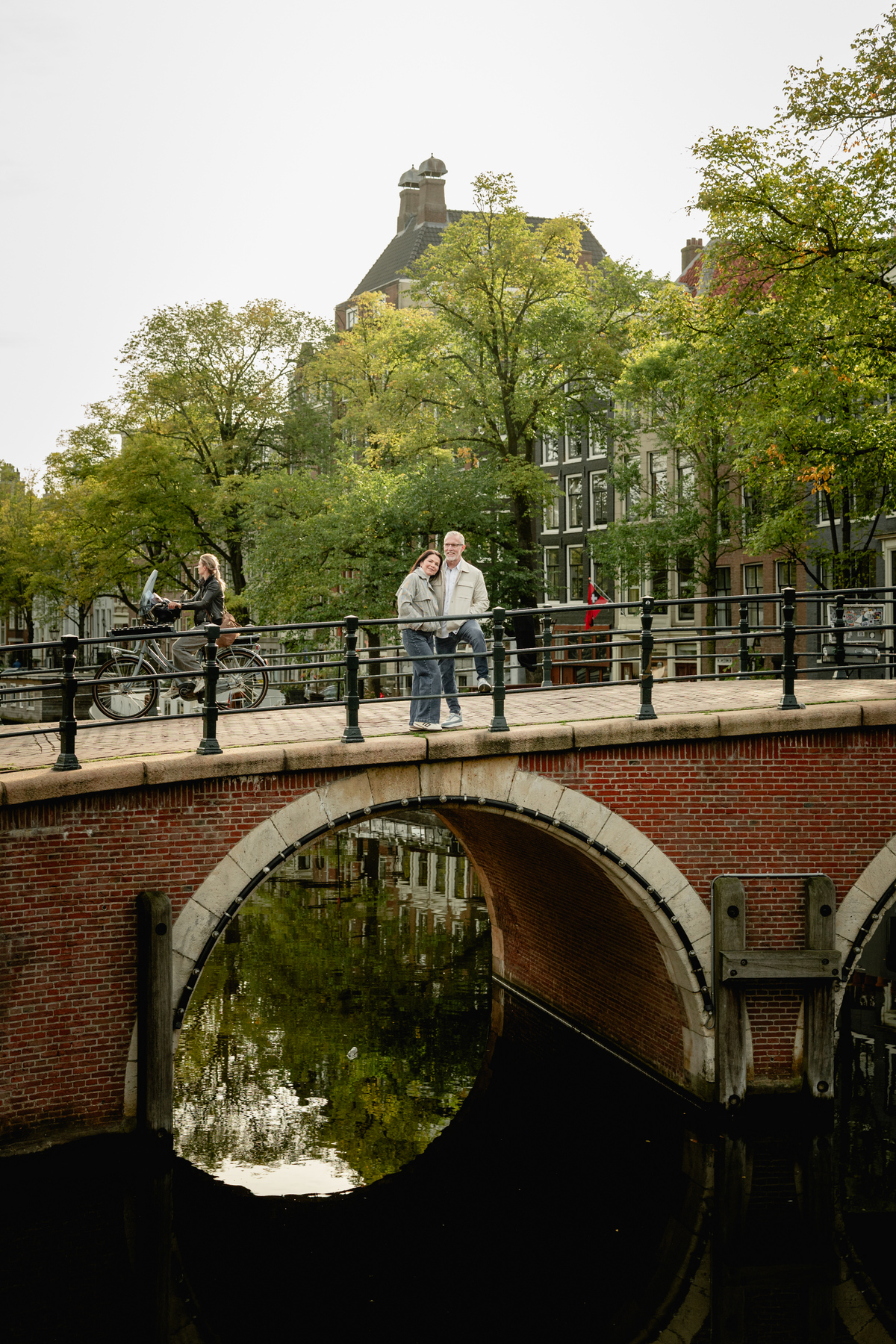 Couple standing on a small brick bridge above an Amsterdam canal.