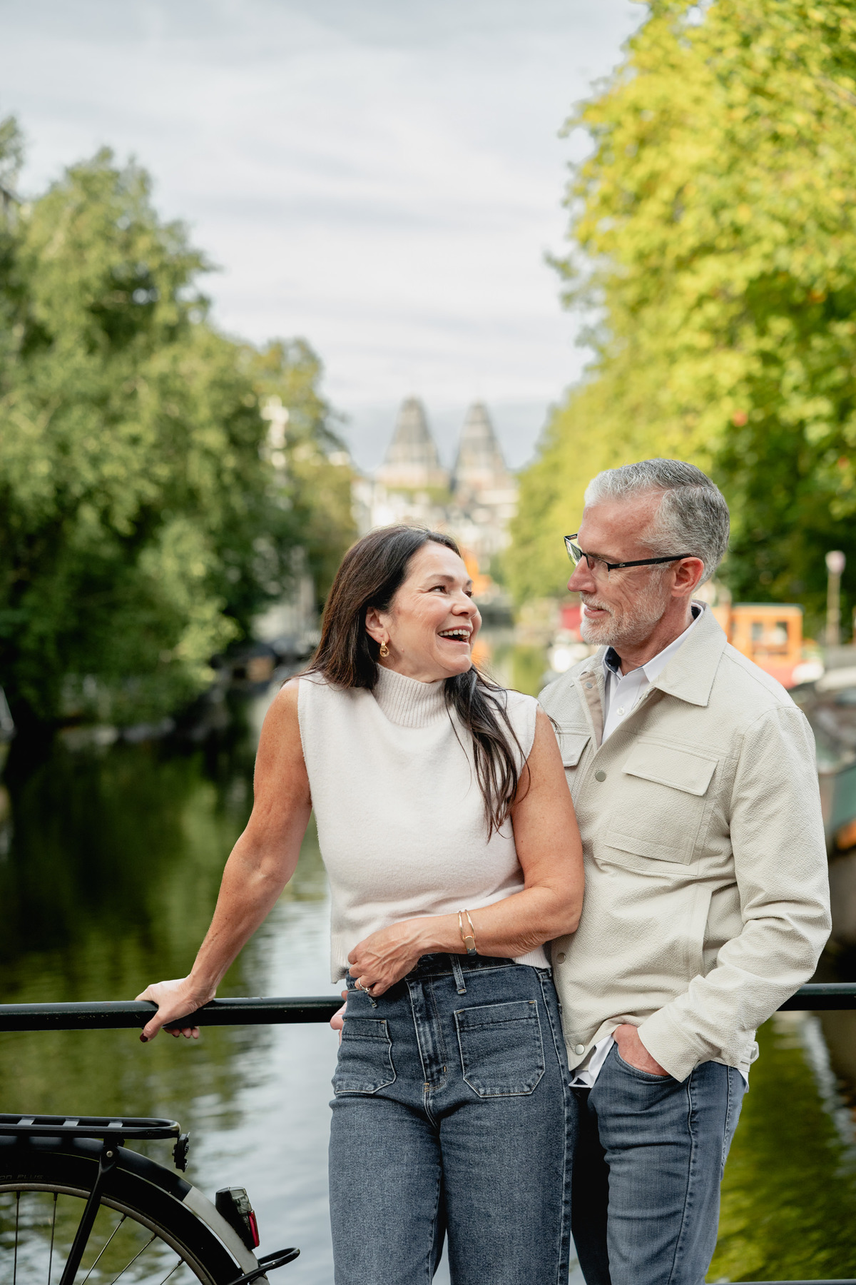 Couple smiling together beside a canal during their first visit to Amsterdam.