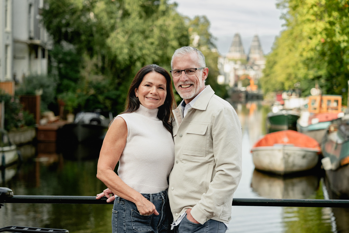 Couple standing close together beside a canal with a small boat behind them.