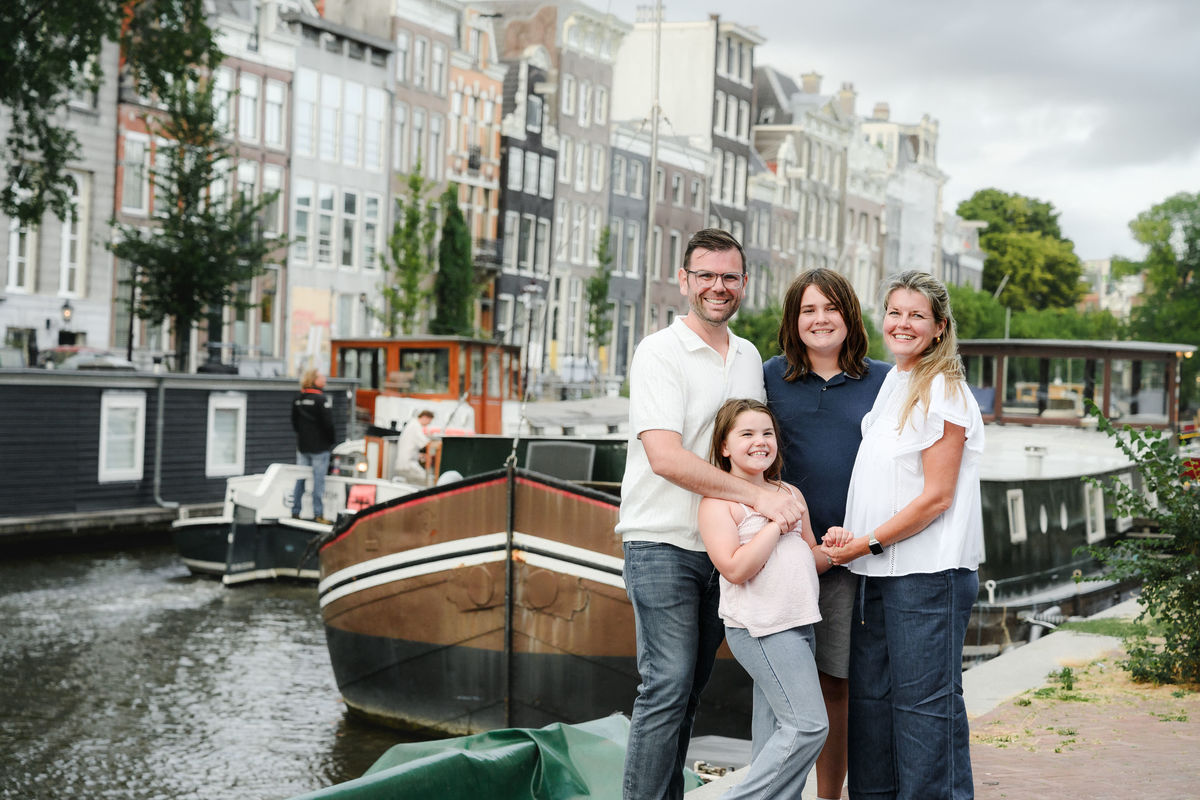 Family standing beside an Amsterdam canal with historic houses in the background.