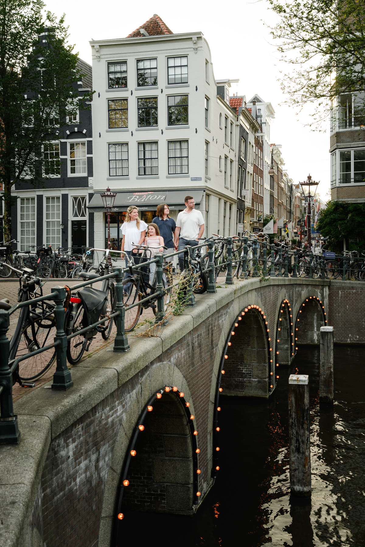 Family walking on an amsterdam canal bridge with bicycles and historic canal houses.