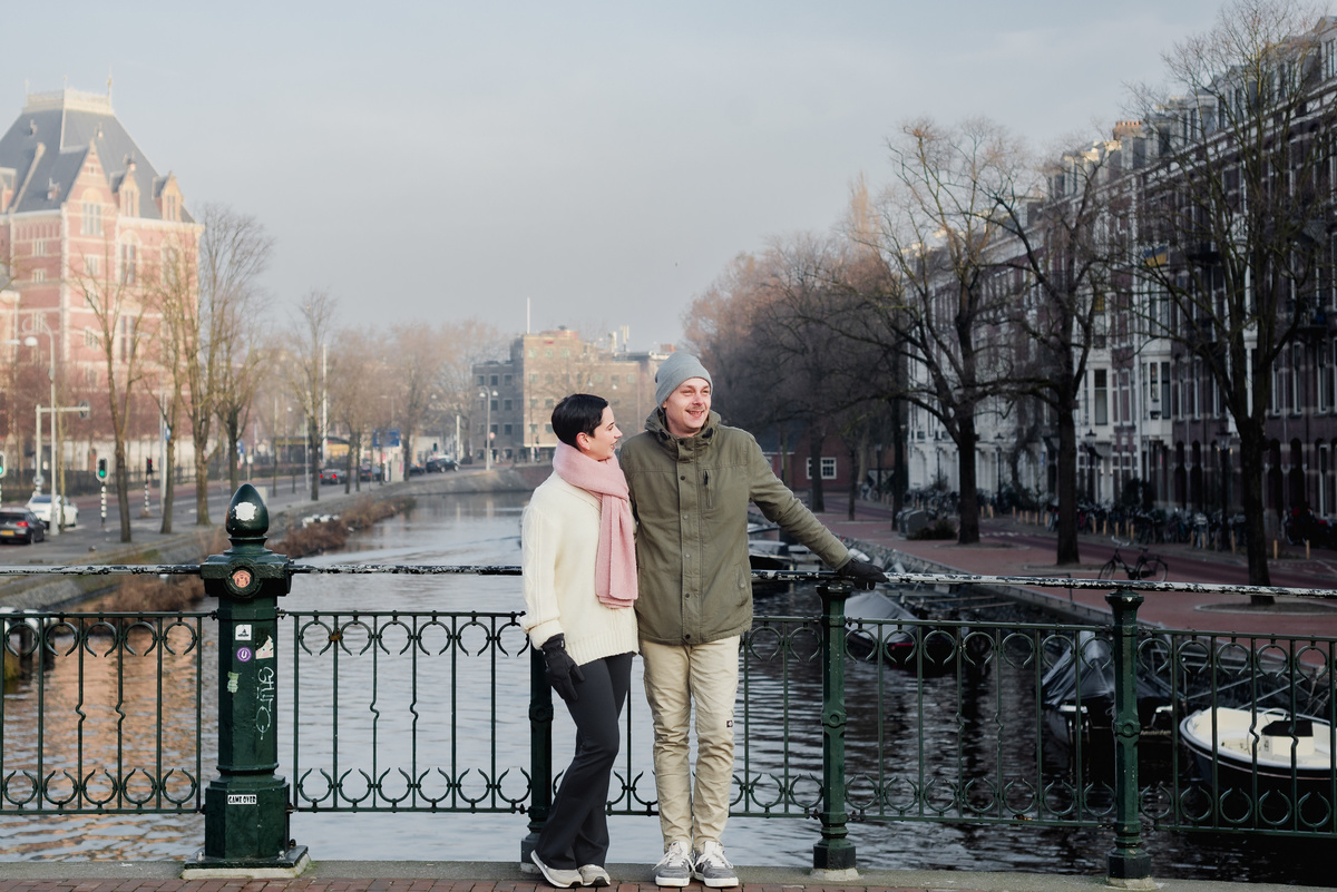 Couple standing together beside an Amsterdam canal in soft winter light.