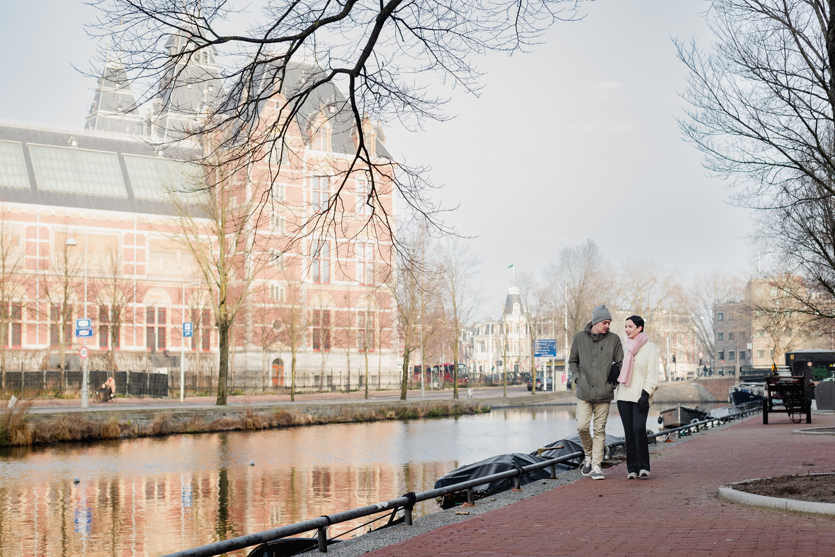 Couple walking beside a canal in Amsterdam with soft winter sunlight.