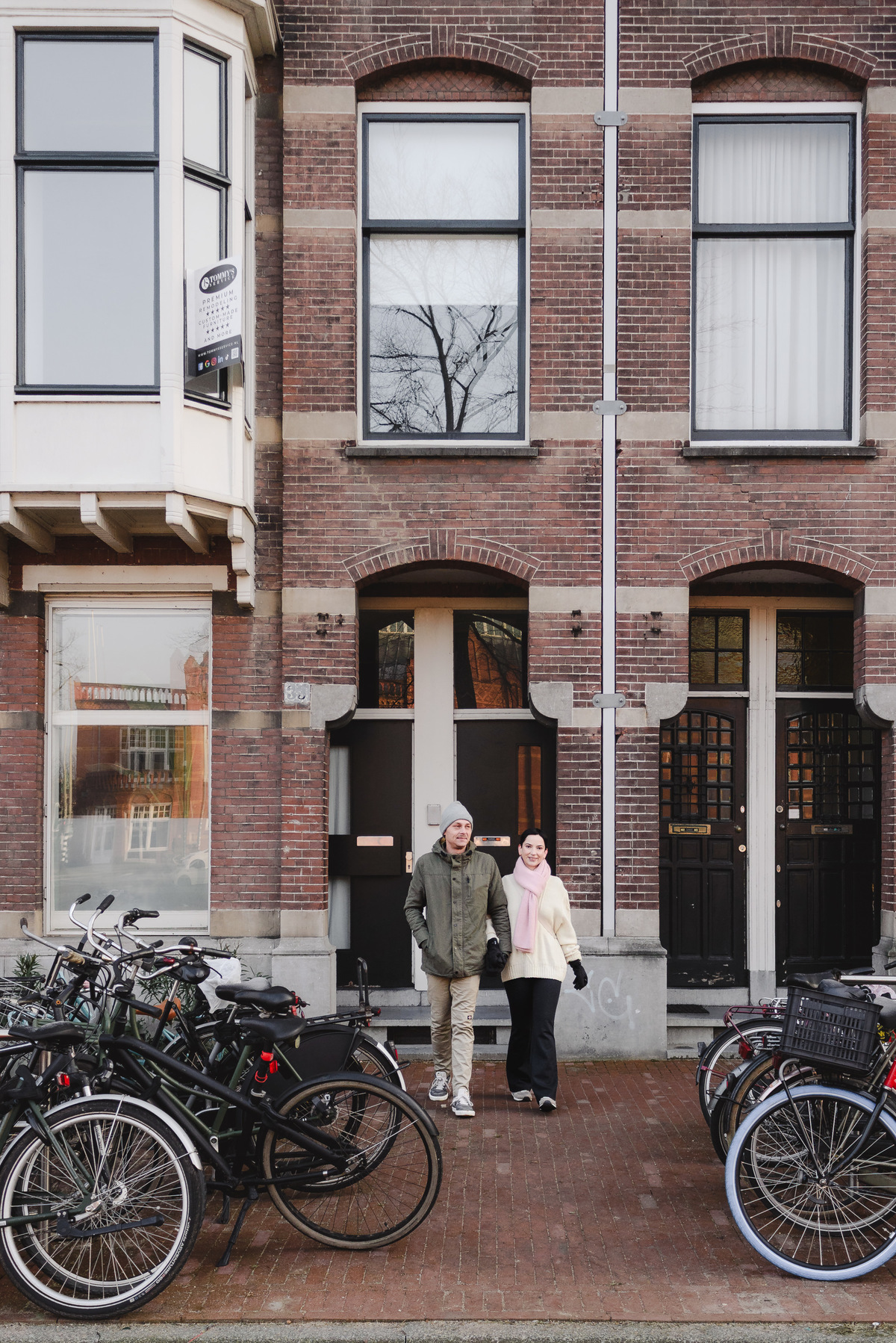 Couple standing outside a tall brick canal house in Amsterdam.