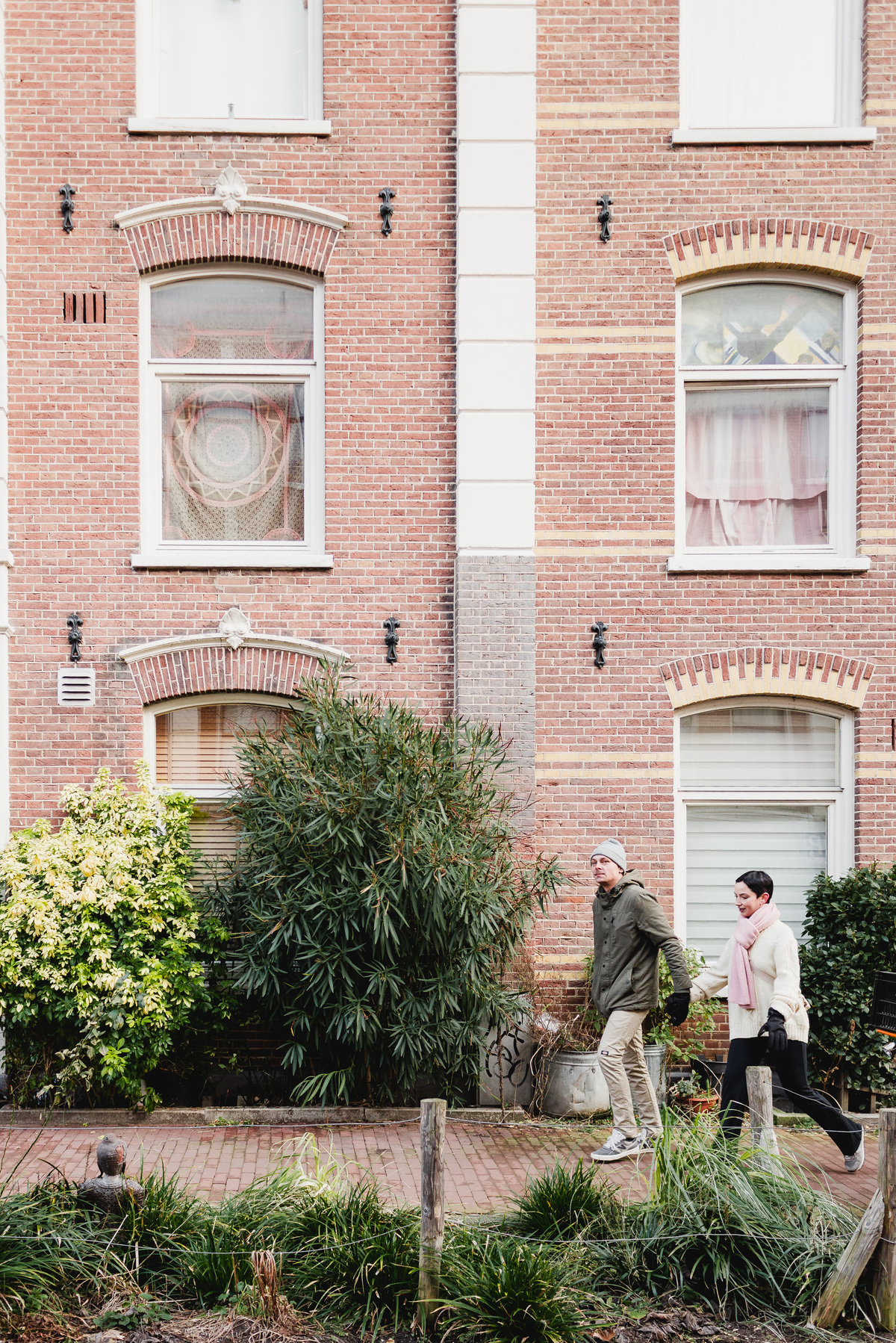 Couple standing together outside a traditional red-brick house in Amsterdam.