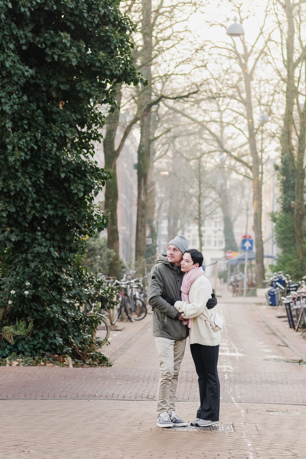 Couple embracing on a tree-lined Amsterdam street in winter.
