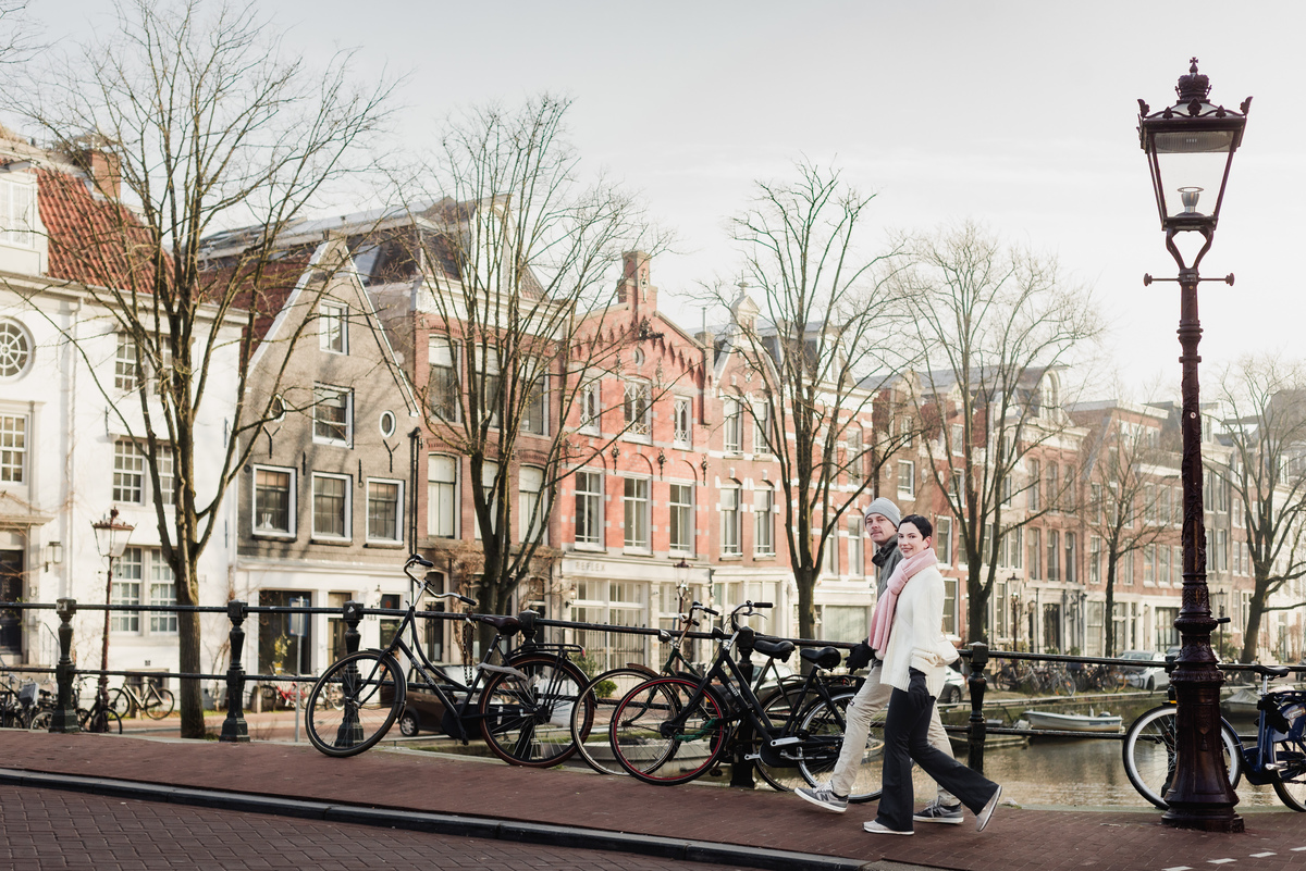 Couple walking across an Amsterdam canal bridge with bicycles in the background.