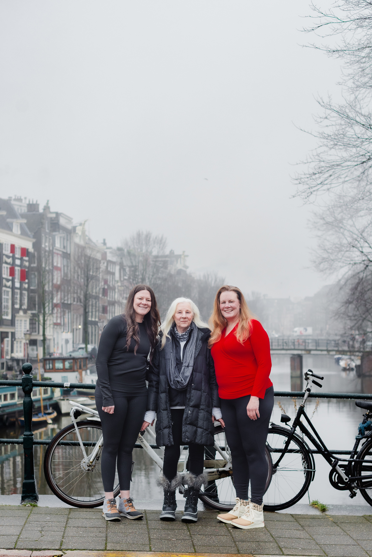 Three women posing together by a canal during a family birthday photo session in Amsterdam.