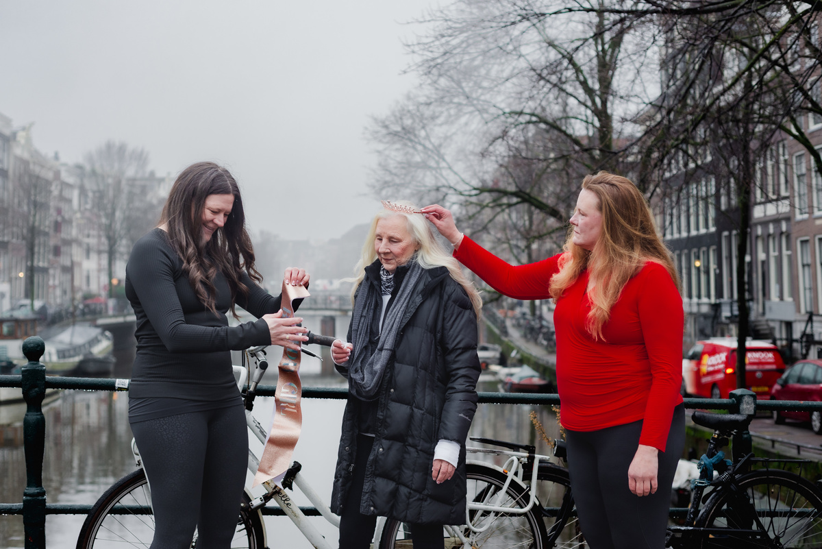 Three women sharing a joyful birthday surprise beside a canal in Amsterdam.