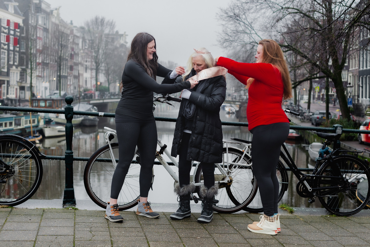 Three women laughing and reaching towards each other during a family photo session in Amsterdam.