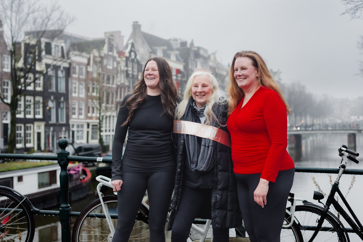 Three women standing together on a canal bridge during a winter family photo session in Amsterdam.