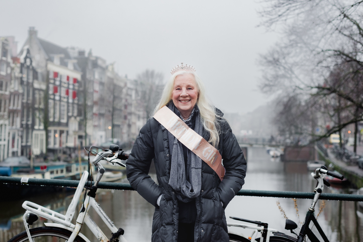 Woman wearing a birthday sash beside an Amsterdam canal on a foggy winter morning.