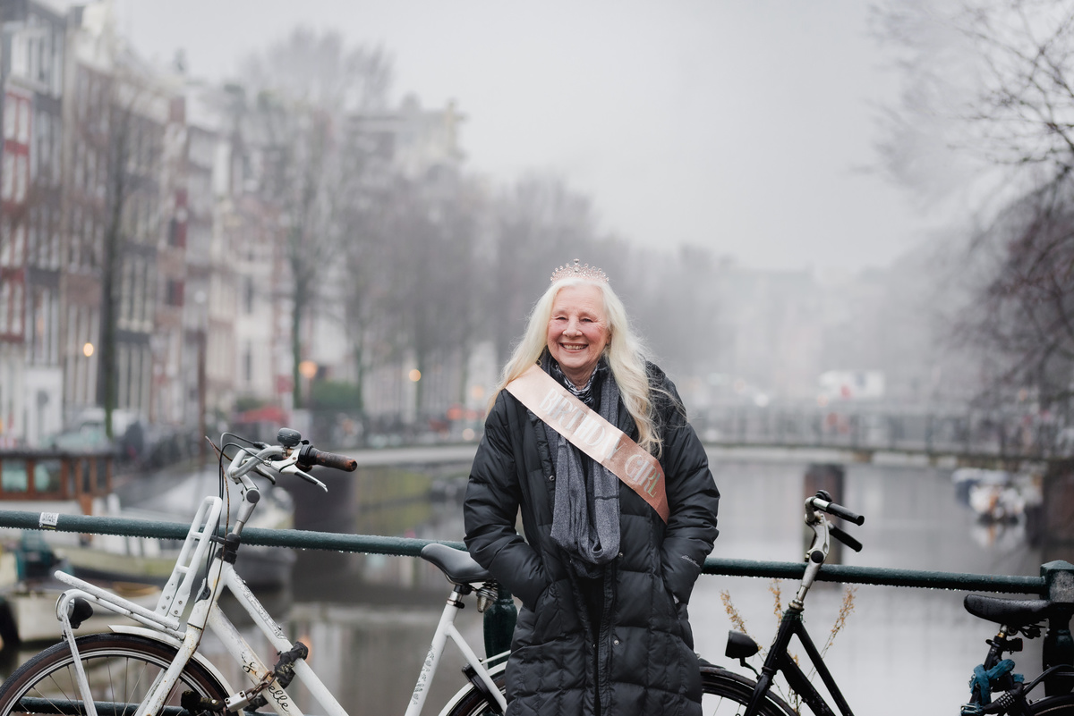 Woman wearing a birthday sash smiling beside an Amsterdam canal and bicycles.