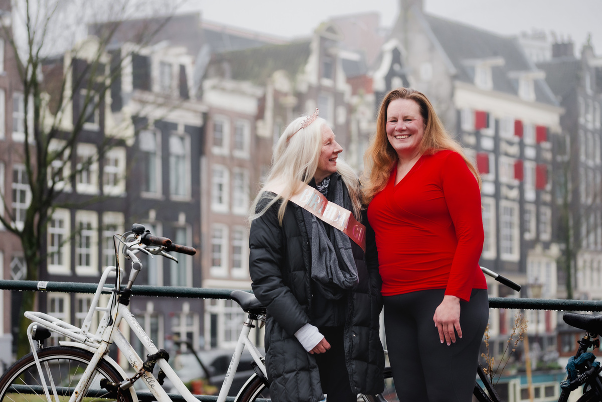 Two women smiling together beside an Amsterdam canal during a family celebration.