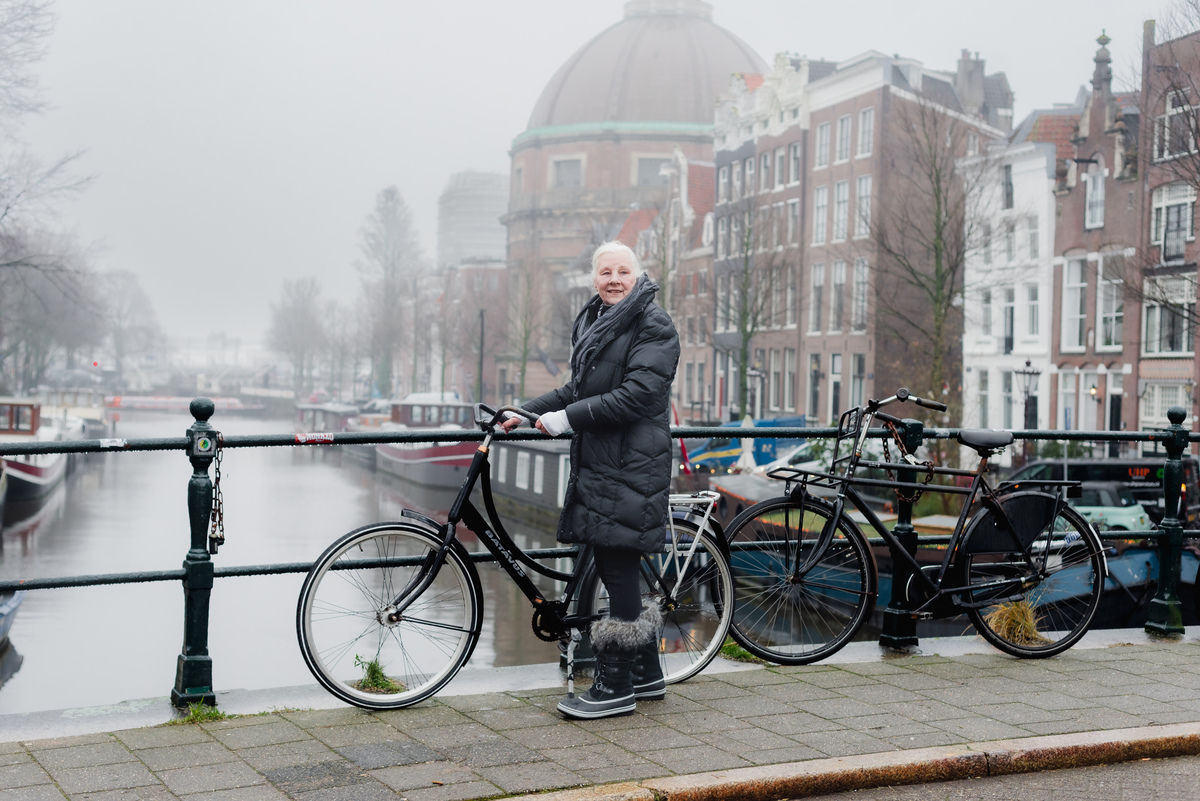 Woman standing beside a canal lined with bicycles and historic Amsterdam houses.